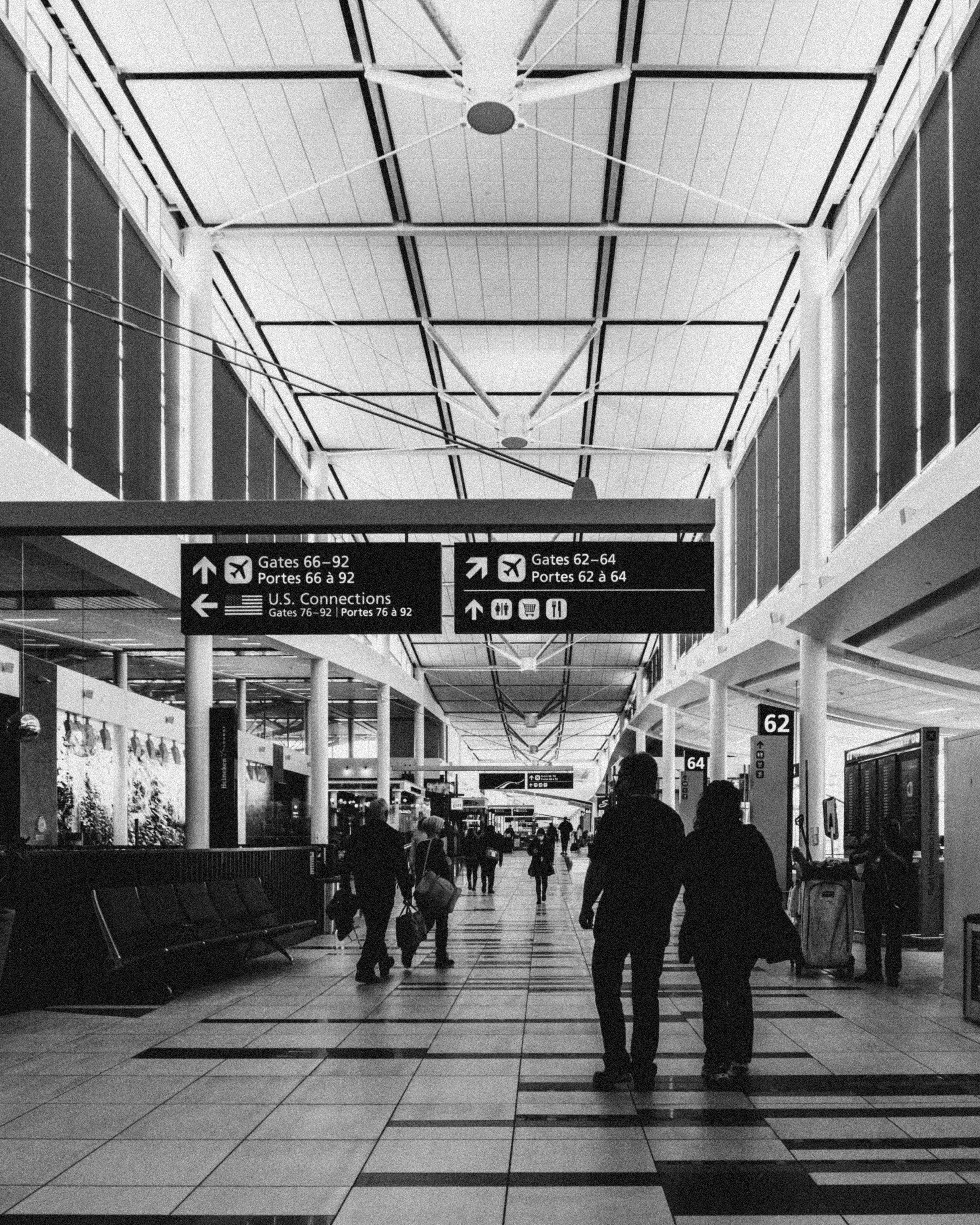 People walking through a busy airport terminal with luggage and signs overhead