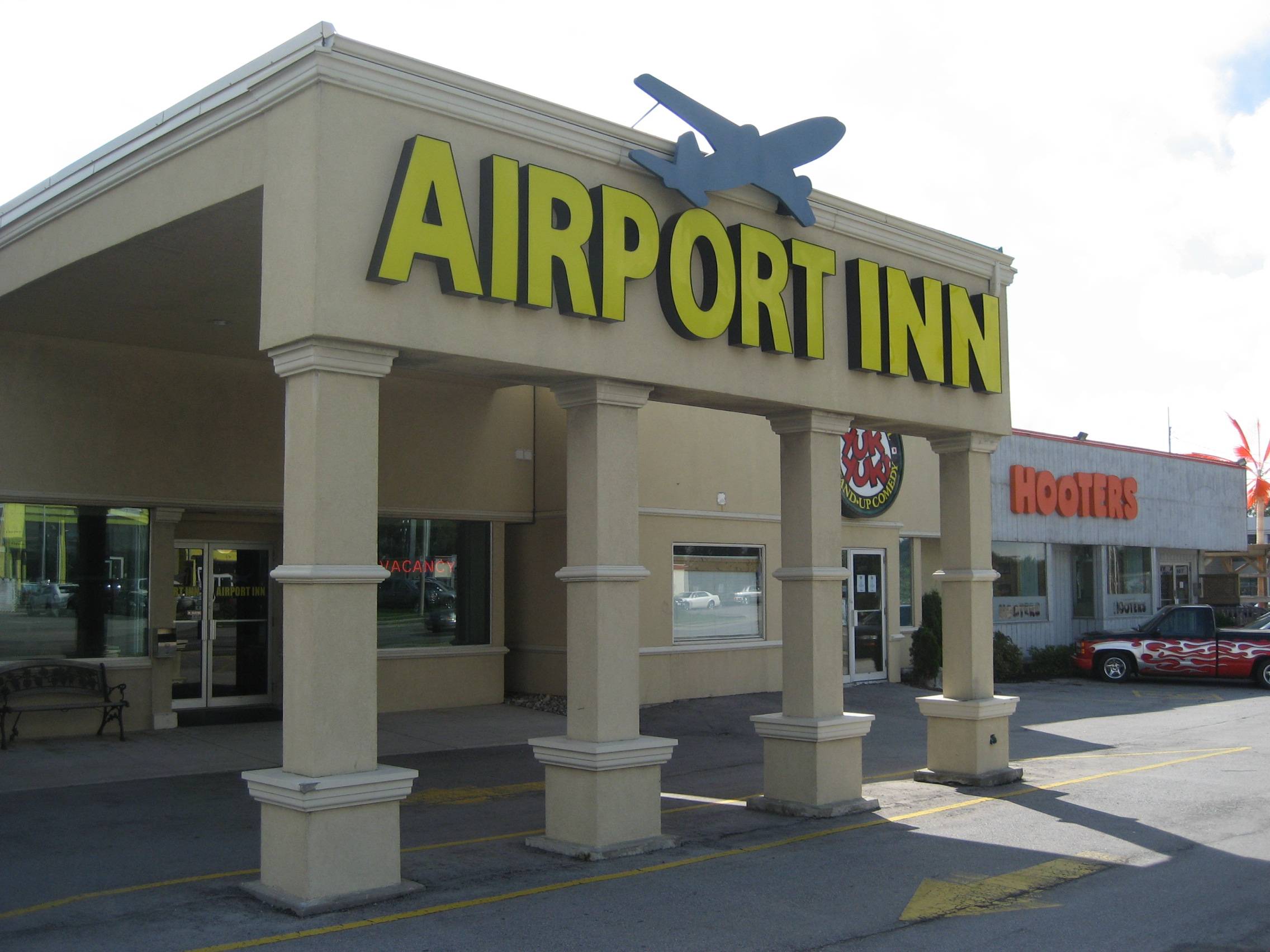 Exterior view of Airport Inn hotel with a clear blue sky and neatly landscaped entrance