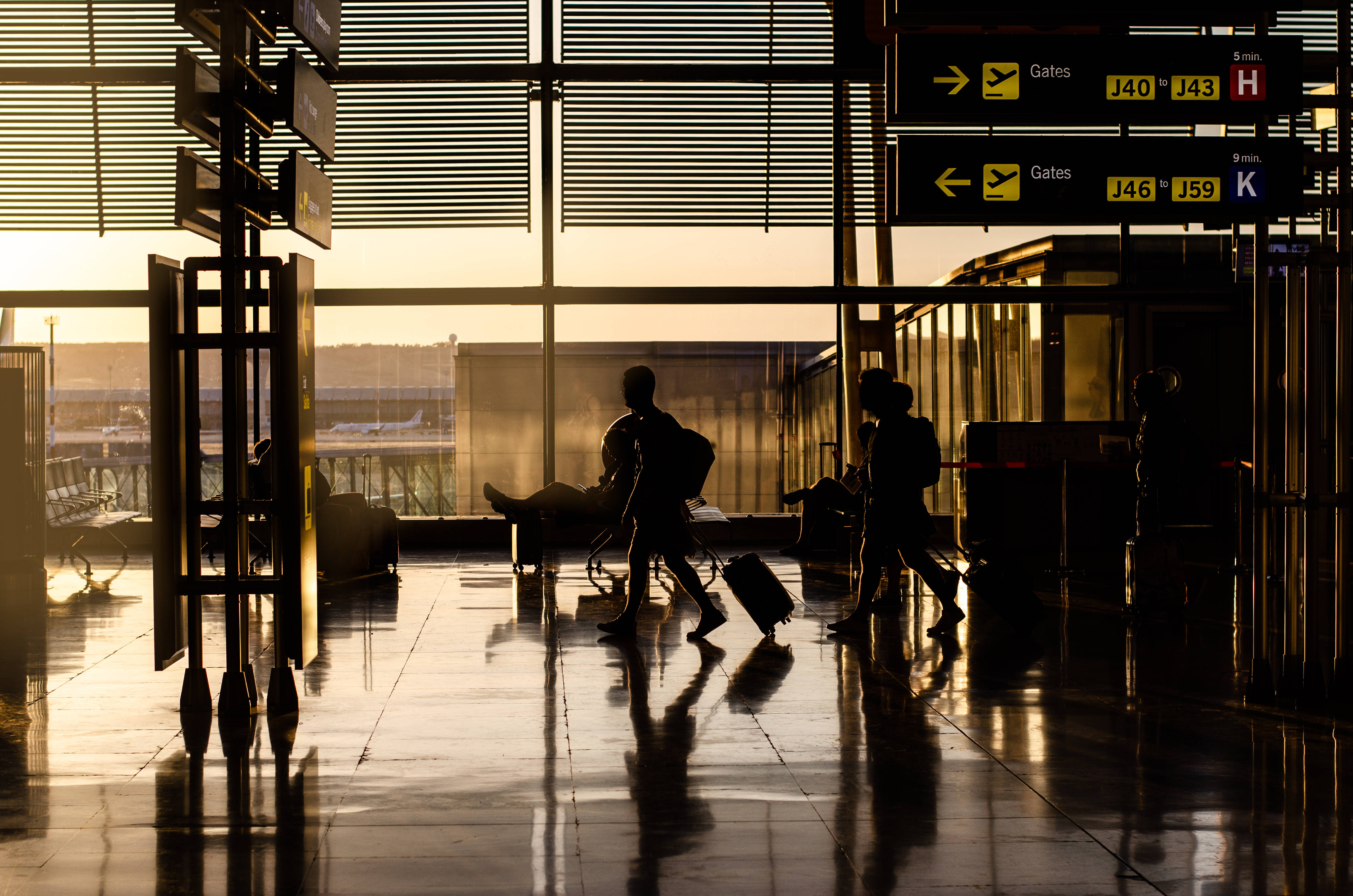 People walking inside an airport terminal with luggage and signs overhead