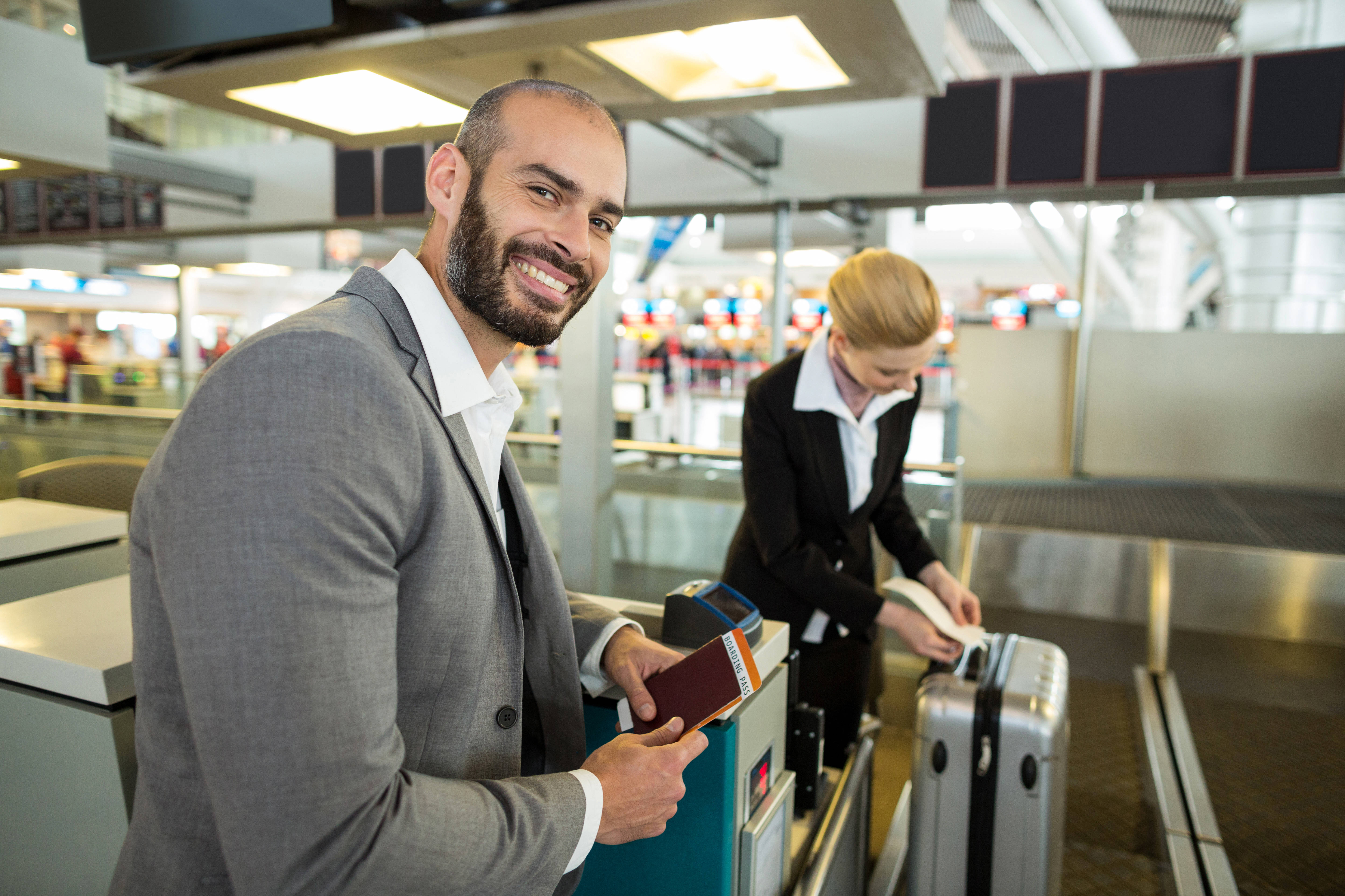 Smiling businessman holding a passport while an airline attendant attaches a tag to his luggage