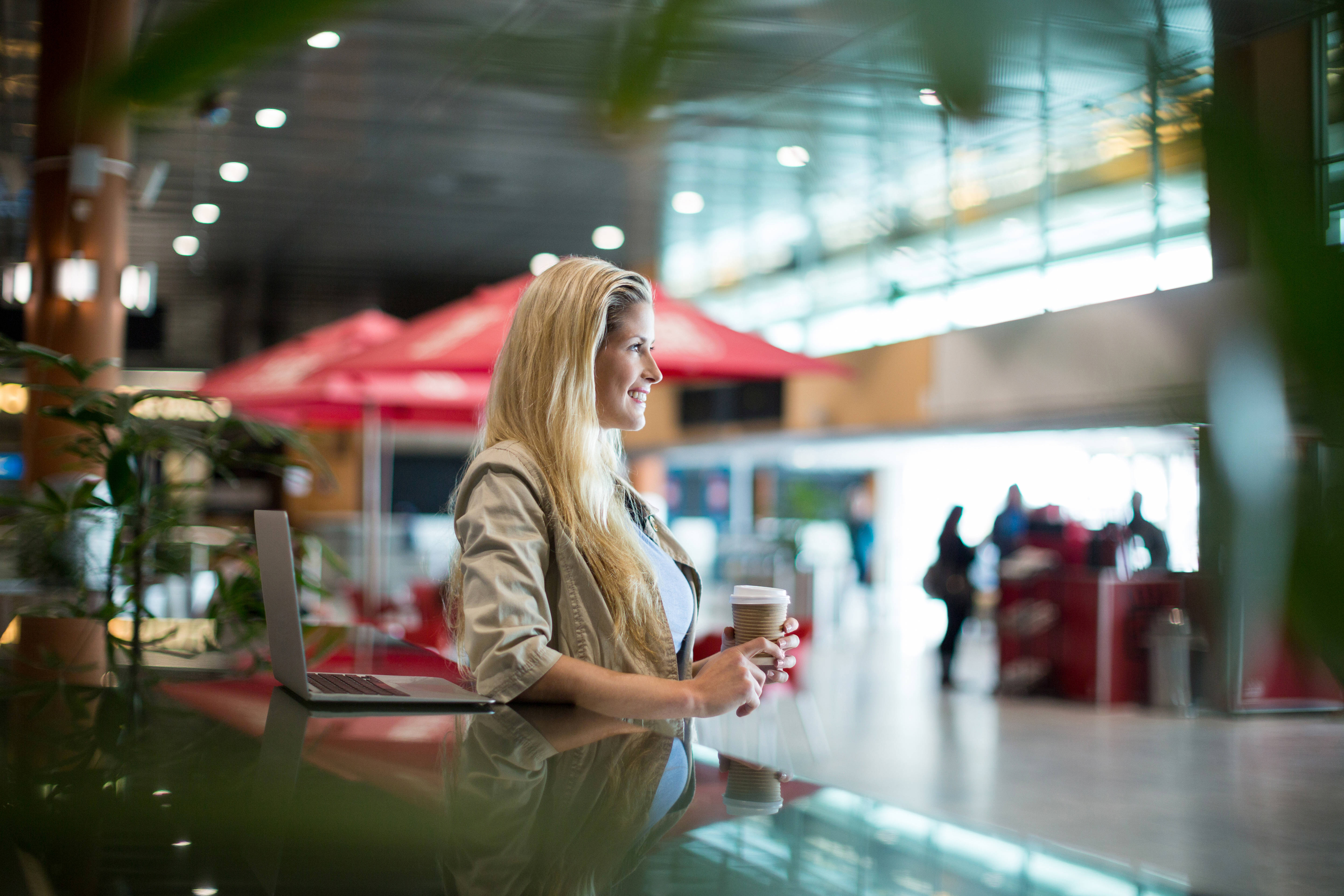 Smiling woman holding a coffee cup while standing in an airport waiting area