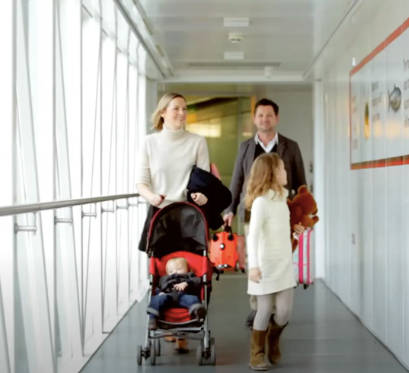 parents with little girl and baby in stroller walk in jetway