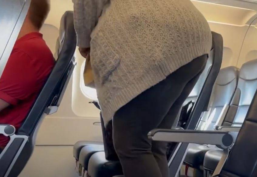 A plus sized passenger getting ready to sit down in a cramped airplane seat